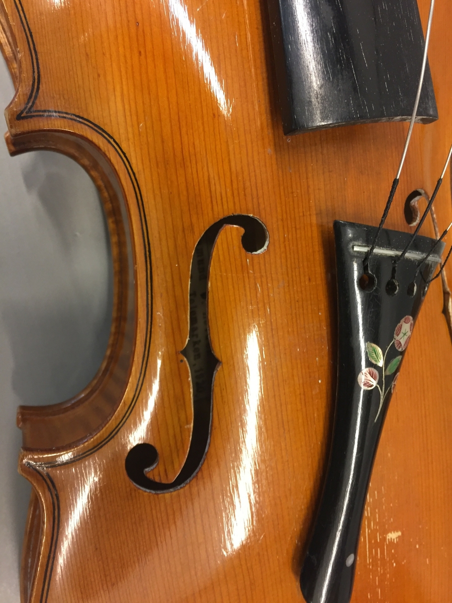 Fiolin med ein rosa blomst til dekor på bakre bru. Inni fela er det lapp med" Guldmedalje i Prorsgrund 1946 Aasmund. Ø .Hovden Telemark reparert 1935". Fiolinen ligg i eit brunt treskrin. Ein liten nøkkel er knytt fast til skrinet.