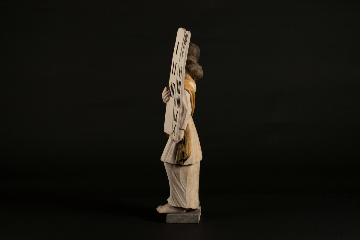 Skulptur av trä från en altaruppsats.
Skulpturen föreställer en man som håller i en tavla med de romerska siffrorna för 1 till och med 12.
Den bibliska gestalt som avbildas är Moses med de tio budorden.