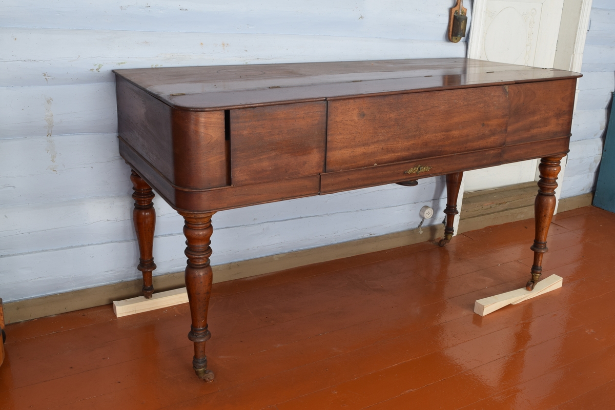 Spinett, taffelpiano i empirestil laget i mahogny. Sterkt beskadiget i strengene. Ukjent fabrikkmerke.