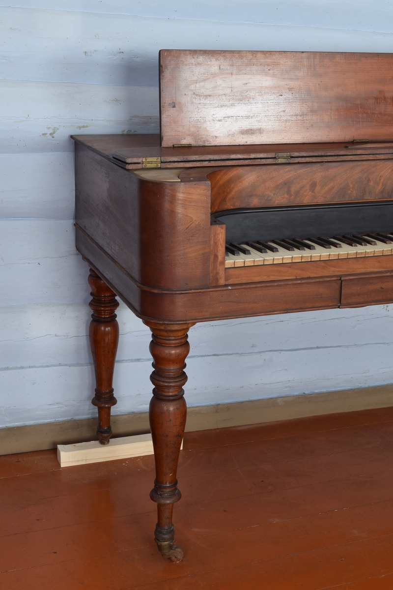 Spinett, taffelpiano i empirestil laget i mahogny. Sterkt beskadiget i strengene. Ukjent fabrikkmerke.