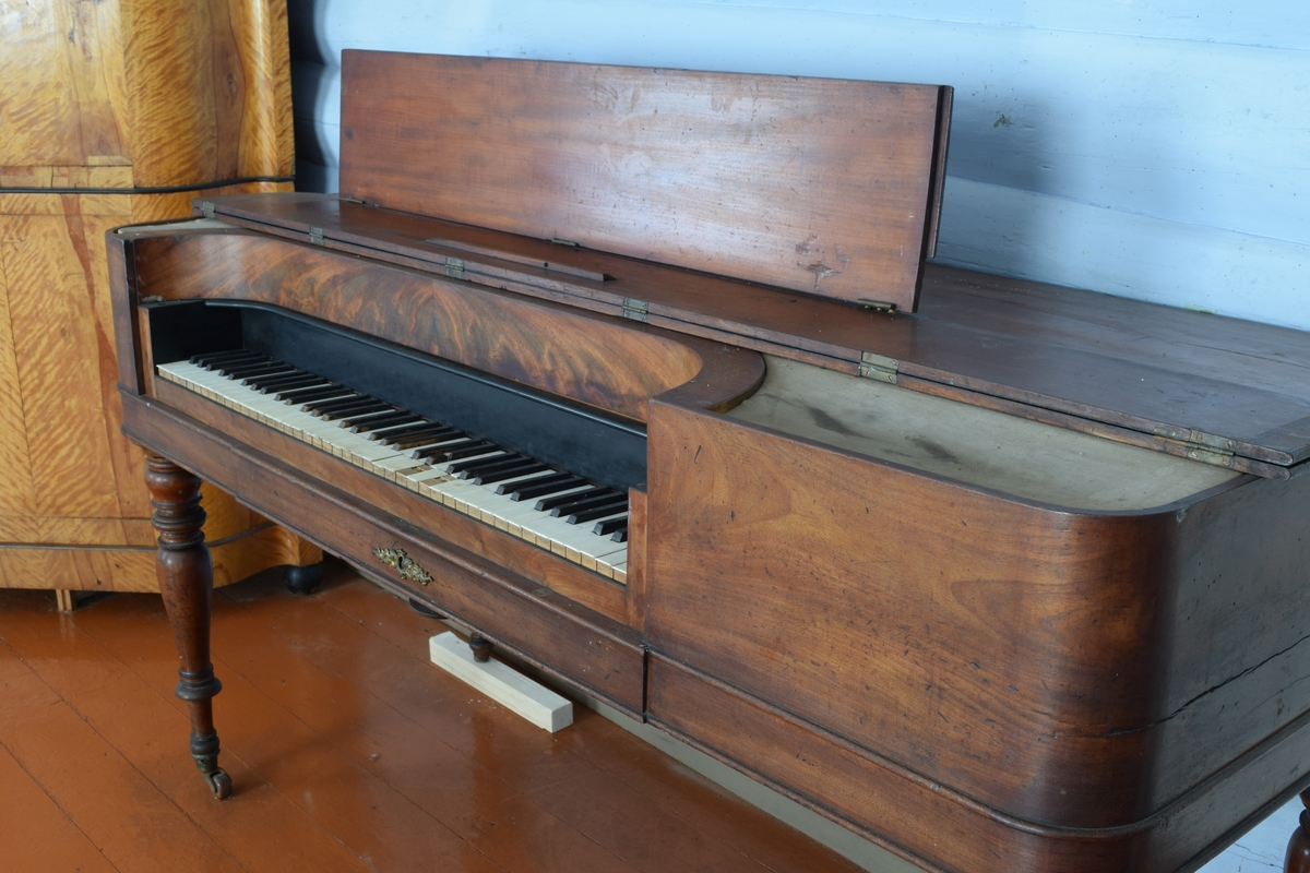 Spinett, taffelpiano i empirestil laget i mahogny. Sterkt beskadiget i strengene. Ukjent fabrikkmerke.