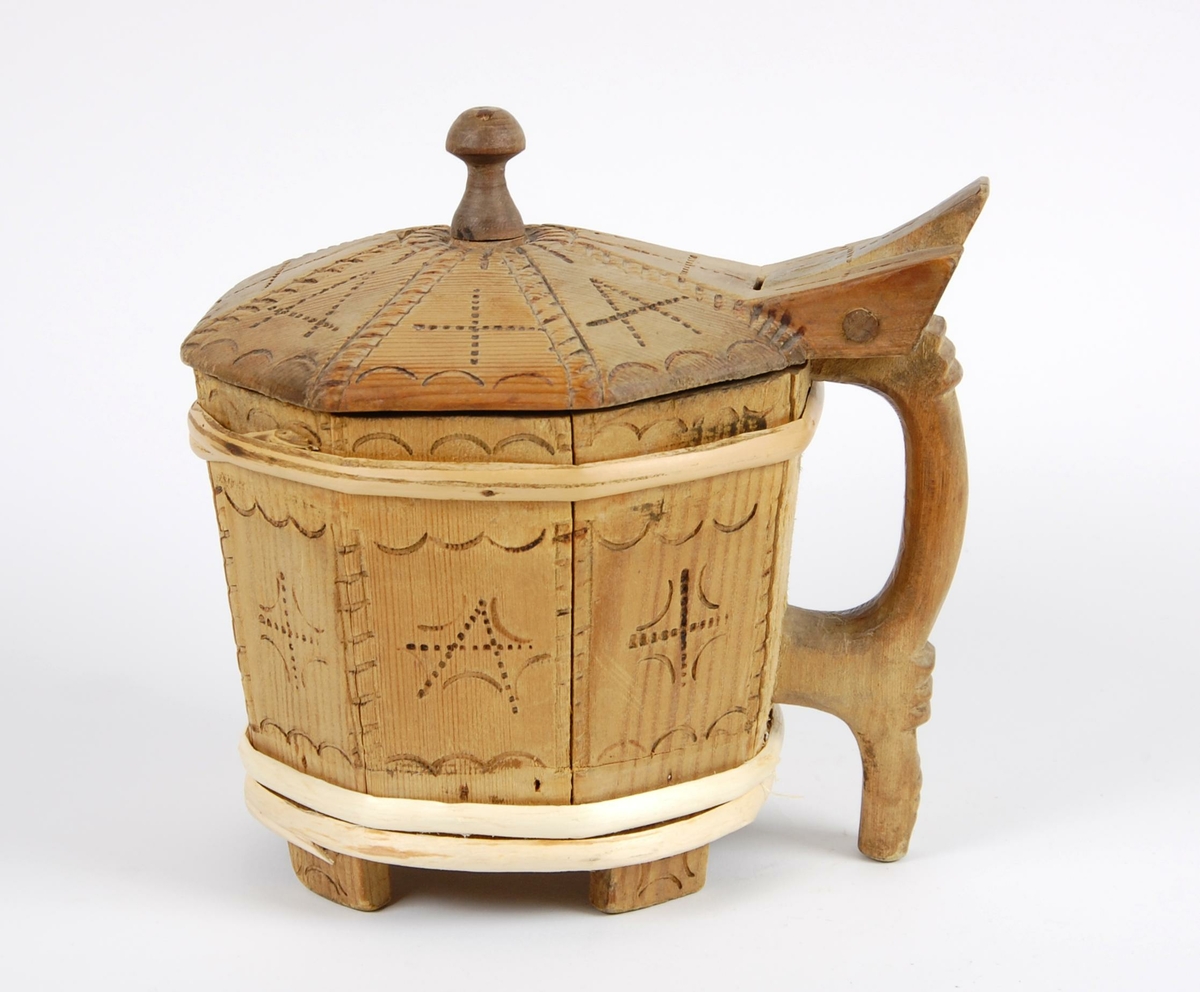 Smørkopp av laggete trestaver. Lokket er åttekantet med innsvidde ornamenter, undersiden av lokk med karveskurdrose. Knotten på lokket er soppformet. Korpus åttekantet, innsvidde ornamenter, en gjording oppe og to nyere gjorder nede. Hanken er skåret i ett med en av stavene. Fire av stavene er forlenget og danner føtter.