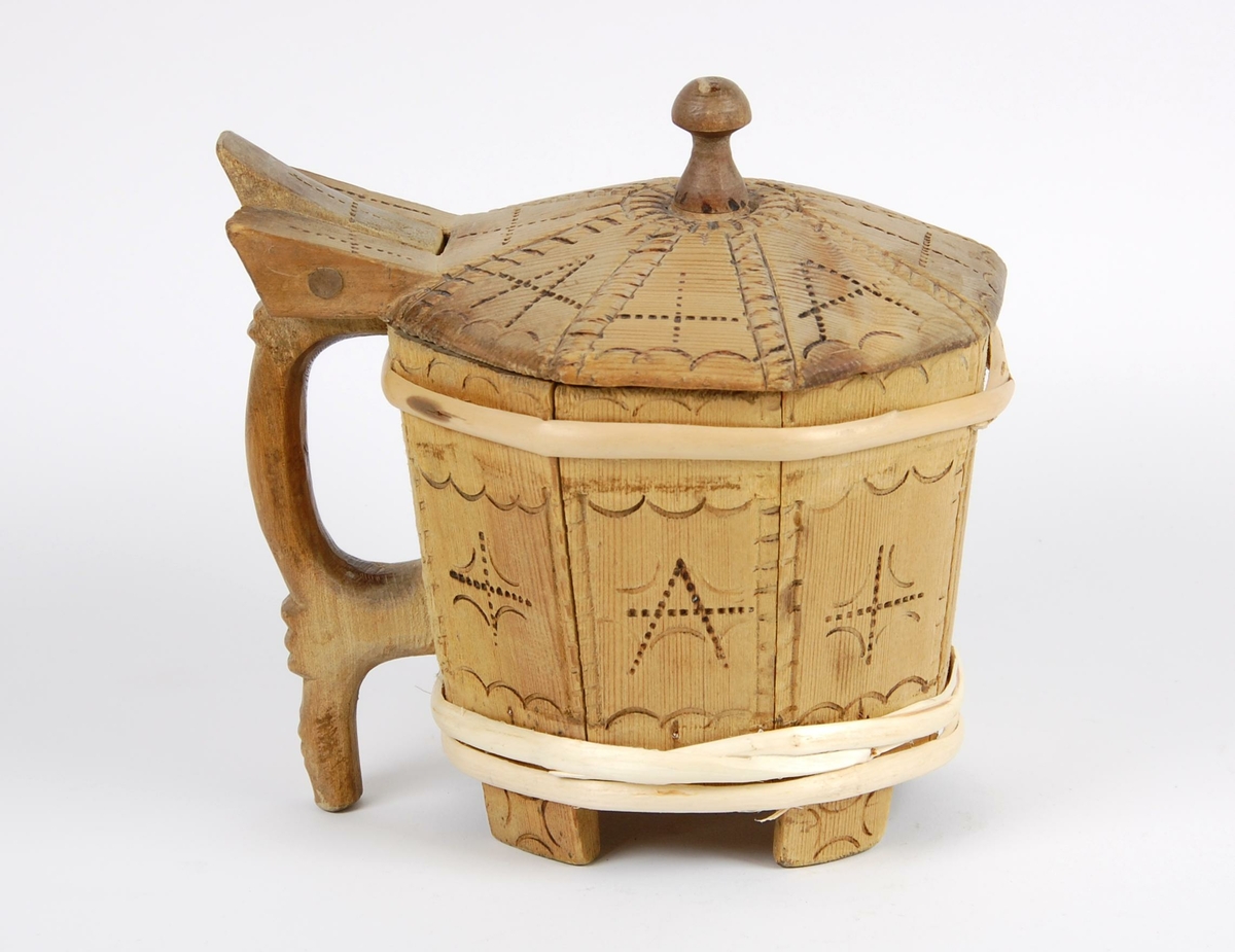 Smørkopp av laggete trestaver. Lokket er åttekantet med innsvidde ornamenter, undersiden av lokk med karveskurdrose. Knotten på lokket er soppformet. Korpus åttekantet, innsvidde ornamenter, en gjording oppe og to nyere gjorder nede. Hanken er skåret i ett med en av stavene. Fire av stavene er forlenget og danner føtter.