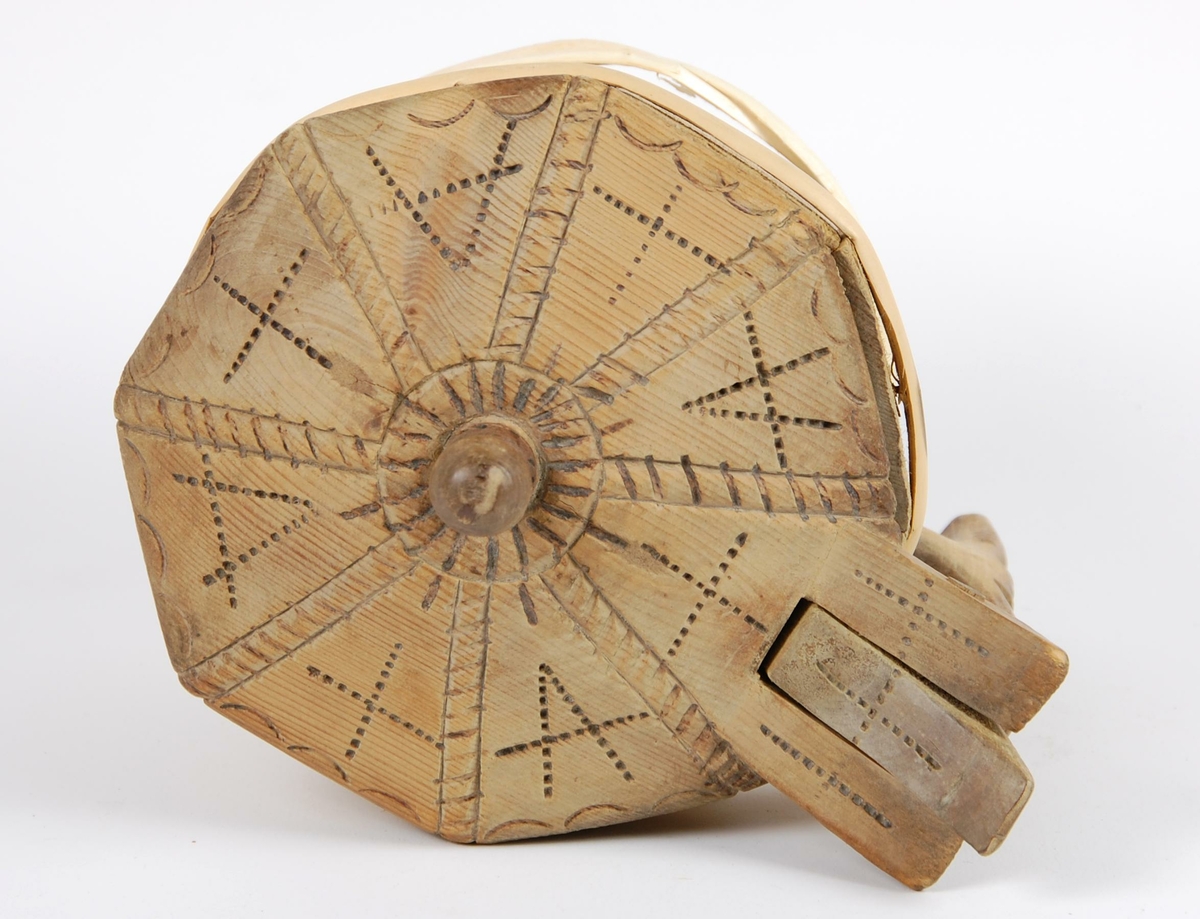 Smørkopp av laggete trestaver. Lokket er åttekantet med innsvidde ornamenter, undersiden av lokk med karveskurdrose. Knotten på lokket er soppformet. Korpus åttekantet, innsvidde ornamenter, en gjording oppe og to nyere gjorder nede. Hanken er skåret i ett med en av stavene. Fire av stavene er forlenget og danner føtter.