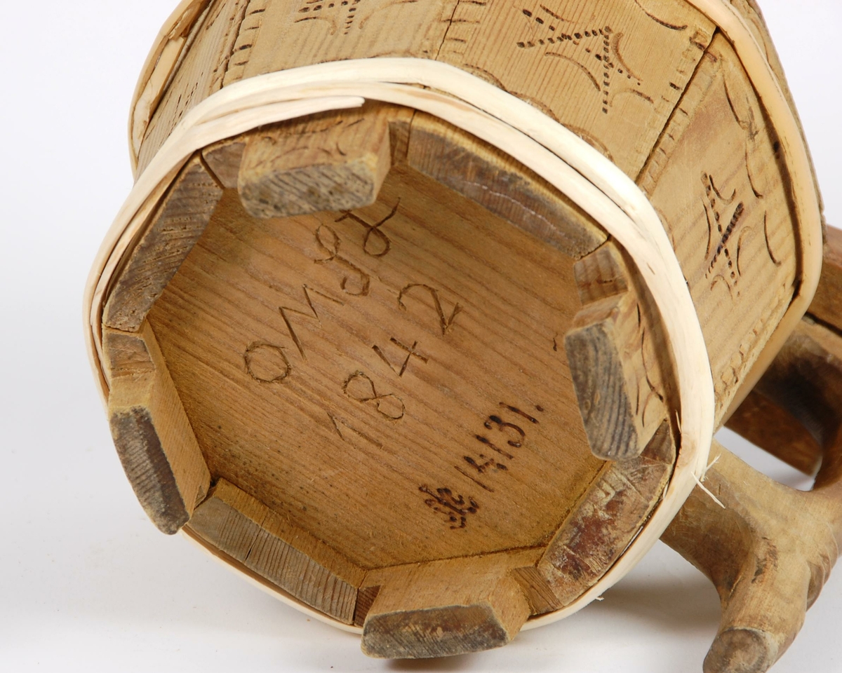 Smørkopp av laggete trestaver. Lokket er åttekantet med innsvidde ornamenter, undersiden av lokk med karveskurdrose. Knotten på lokket er soppformet. Korpus åttekantet, innsvidde ornamenter, en gjording oppe og to nyere gjorder nede. Hanken er skåret i ett med en av stavene. Fire av stavene er forlenget og danner føtter.