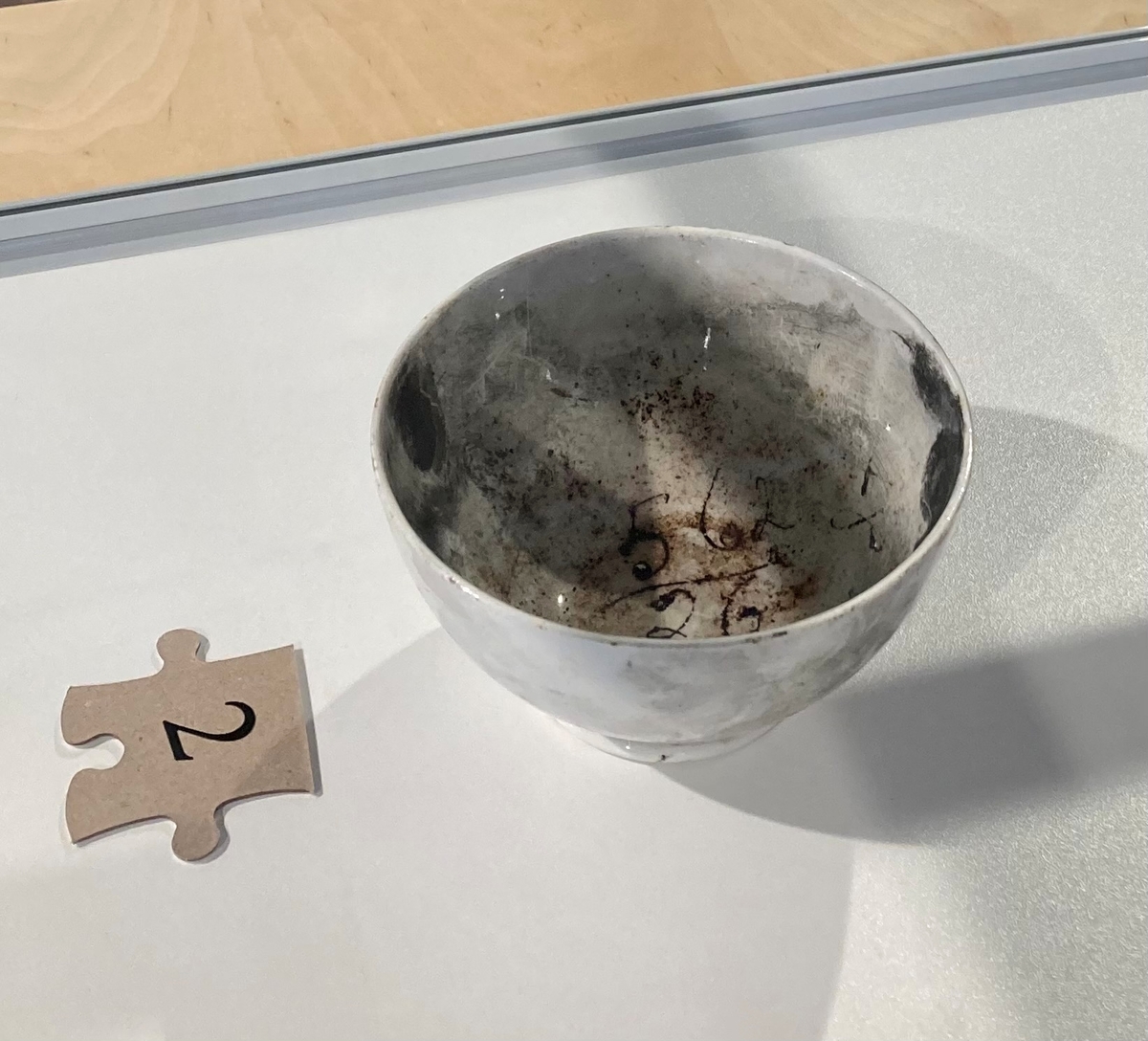 Rund, hvit drikkebolle i porselen. Fremkalte fingeravtrykk på innsiden og utsiden. (Bollen er midt på bildet.)