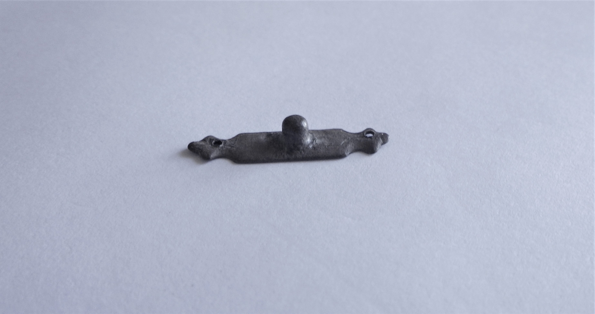 MALV: L. 24, 5  B. 6 MM, REKTANGULÆRT MED HULL I HVER ENDE SOM ER 3-KLØVER-BLADFORMET. EN KNOTT I MIDTEN. 