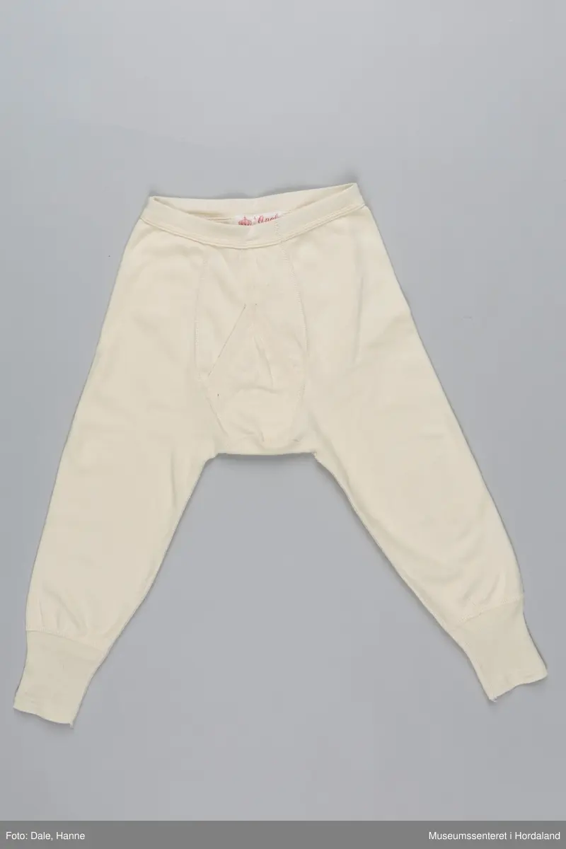 Underbukse med bråt i liv og på bein, gylf, hull ved hoftene, hull til snøring på innsiden av livbråt og korte bein.
Den er pakka i rektangulær plastemballasje med ileggspapp.