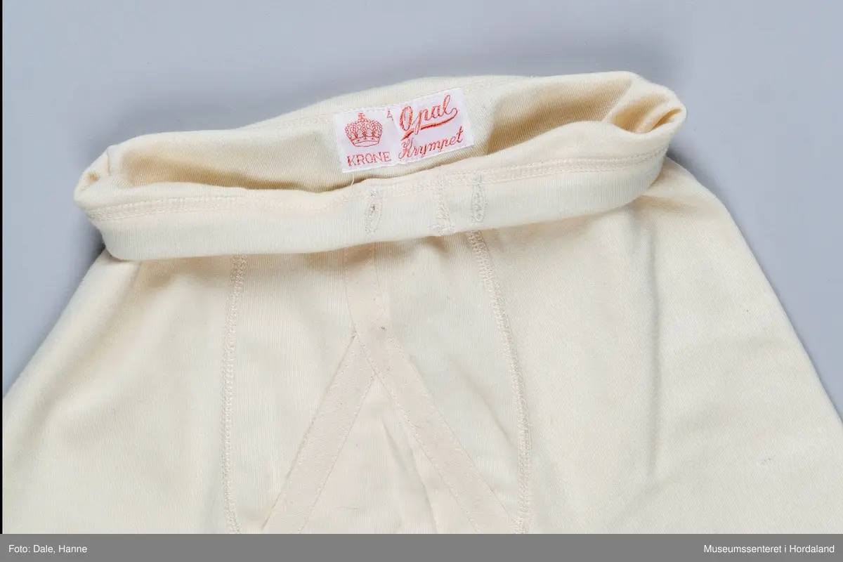 Underbukse med bråt i liv og på bein, gylf, hull ved hoftene, hull til snøring på innsiden av livbråt og korte bein.
Den er pakka i rektangulær plastemballasje med ileggspapp.