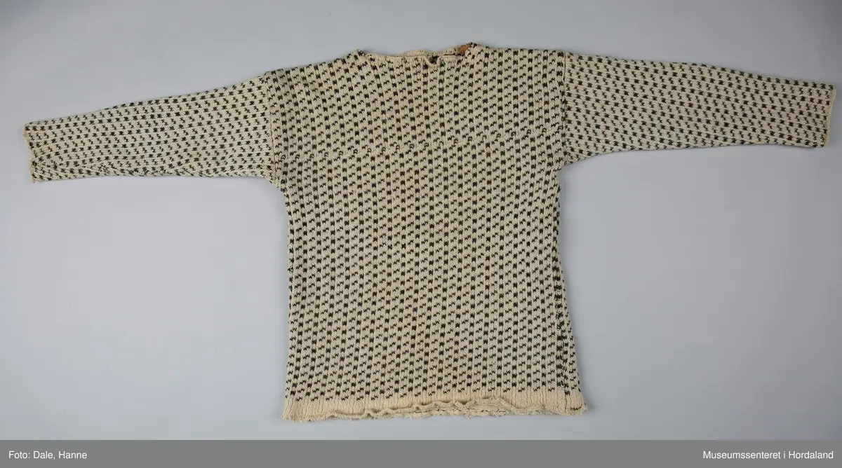 Strikka naturfarga ullgenser med koksgrått klassisk islendermønster. Merkelapp "Pedek - norsk ull" (str. 46) i halsopningen. Hals- og ermeopningane er hekla over med naturfarga garn som reparasjon, og det er festa skinnlappar på kvar side av halsen på innsida av genseren. Venstre albogen er stoppa. Etter lang bruk har genseren begynt å rakne litt i nedre kant, og nokre masker enkelte andre stadar.