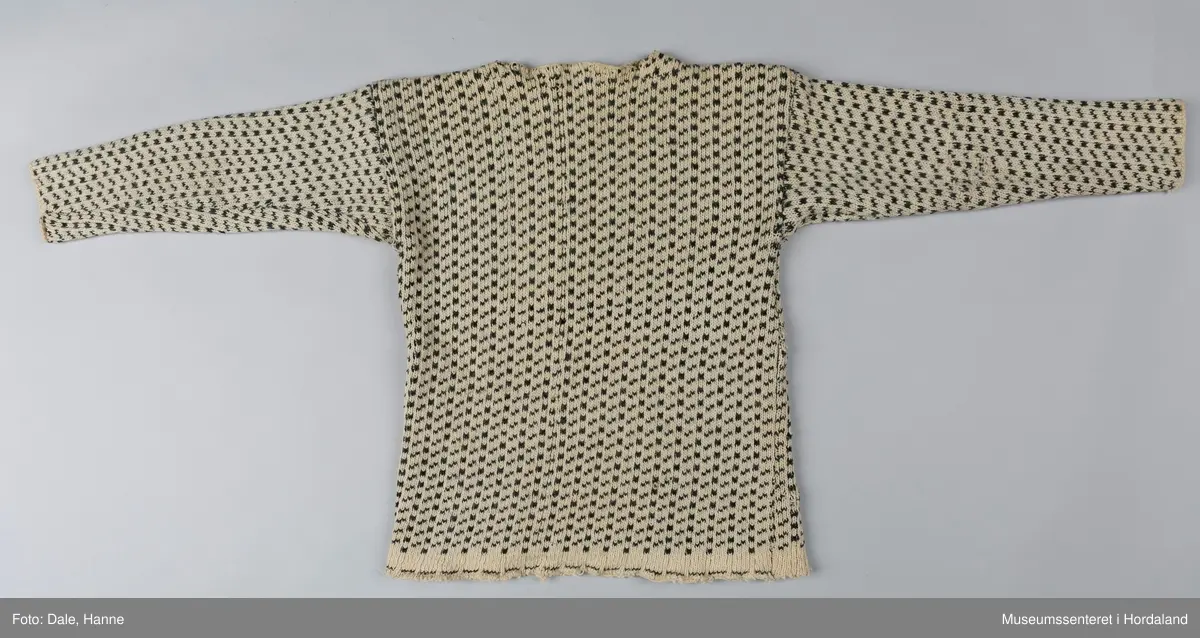 Strikka naturfarga ullgenser med koksgrått klassisk islendermønster. Merkelapp "Pedek - norsk ull" (str. 46) i halsopningen. Hals- og ermeopningane er hekla over med naturfarga garn som reparasjon, og det er festa skinnlappar på kvar side av halsen på innsida av genseren. Venstre albogen er stoppa. Etter lang bruk har genseren begynt å rakne litt i nedre kant, og nokre masker enkelte andre stadar.