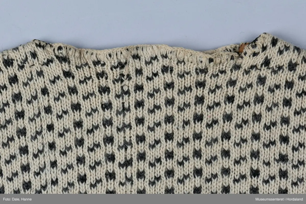 Strikka naturfarga ullgenser med koksgrått klassisk islendermønster. Merkelapp "Pedek - norsk ull" (str. 46) i halsopningen. Hals- og ermeopningane er hekla over med naturfarga garn som reparasjon, og det er festa skinnlappar på kvar side av halsen på innsida av genseren. Venstre albogen er stoppa. Etter lang bruk har genseren begynt å rakne litt i nedre kant, og nokre masker enkelte andre stadar.