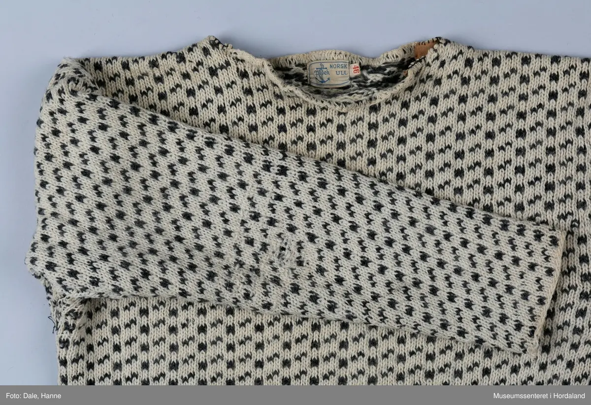 Strikka naturfarga ullgenser med koksgrått klassisk islendermønster. Merkelapp "Pedek - norsk ull" (str. 46) i halsopningen. Hals- og ermeopningane er hekla over med naturfarga garn som reparasjon, og det er festa skinnlappar på kvar side av halsen på innsida av genseren. Venstre albogen er stoppa. Etter lang bruk har genseren begynt å rakne litt i nedre kant, og nokre masker enkelte andre stadar.