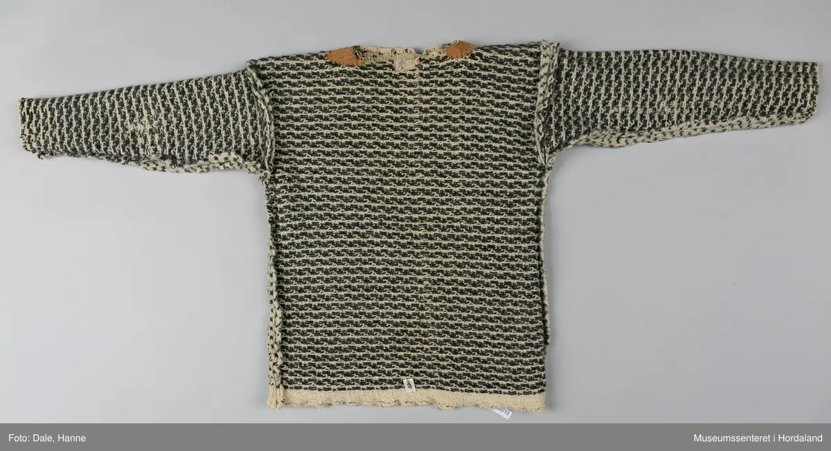 Strikka naturfarga ullgenser med koksgrått klassisk islendermønster. Merkelapp "Pedek - norsk ull" (str. 46) i halsopningen. Hals- og ermeopningane er hekla over med naturfarga garn som reparasjon, og det er festa skinnlappar på kvar side av halsen på innsida av genseren. Venstre albogen er stoppa. Etter lang bruk har genseren begynt å rakne litt i nedre kant, og nokre masker enkelte andre stadar.