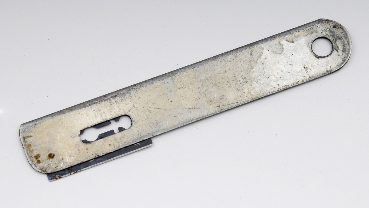 To mulige tapetkniver eller skjæreverktøy. Kniven består av et tynt, linjalformet metallstykke med rom for å føre inn et barberblad i den ene enden. I den andre enden er det et hull, muligsens til å henge opp kniven etter.