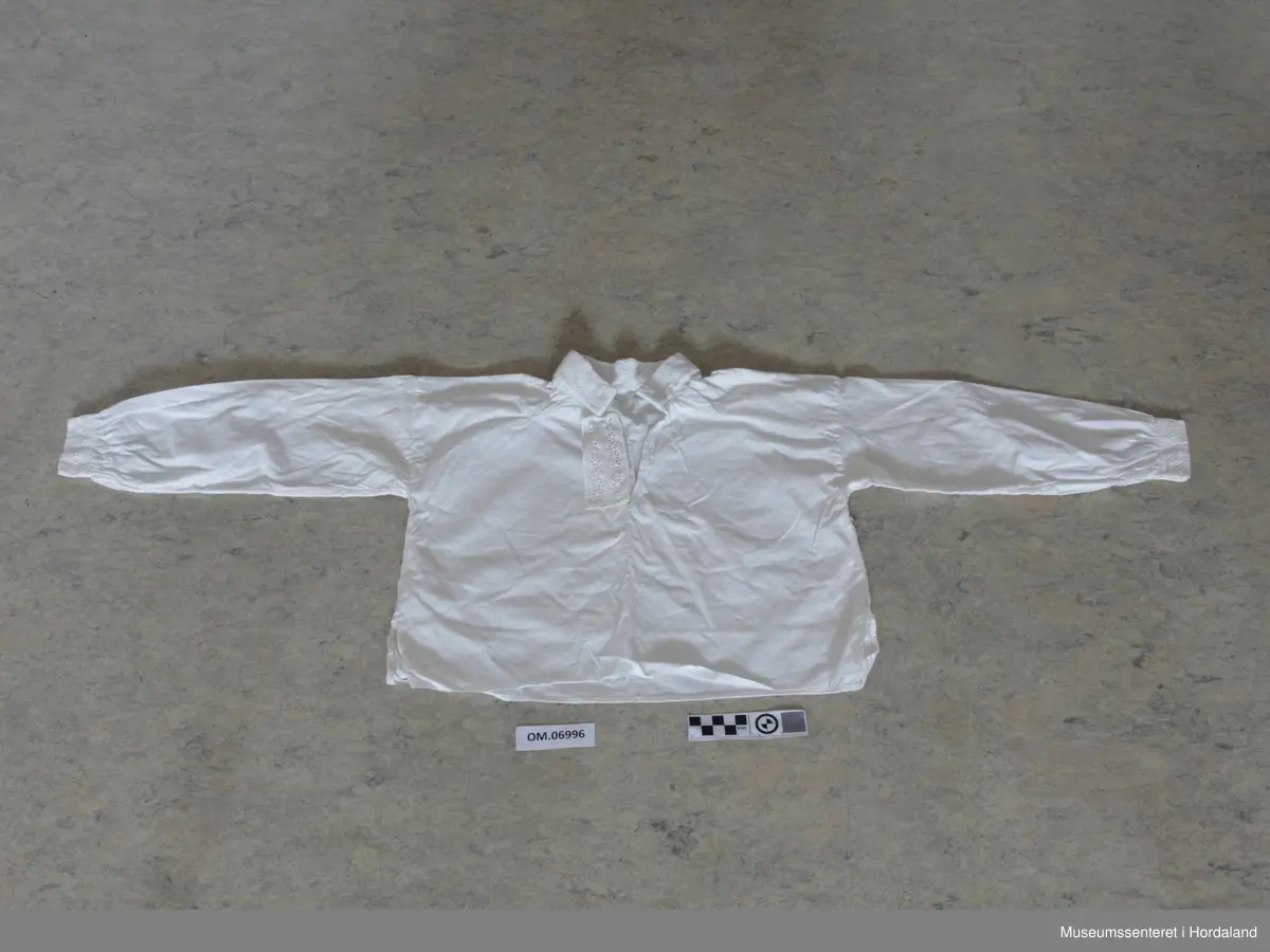 kvitsaum i halslinning, blondekant i bringa.