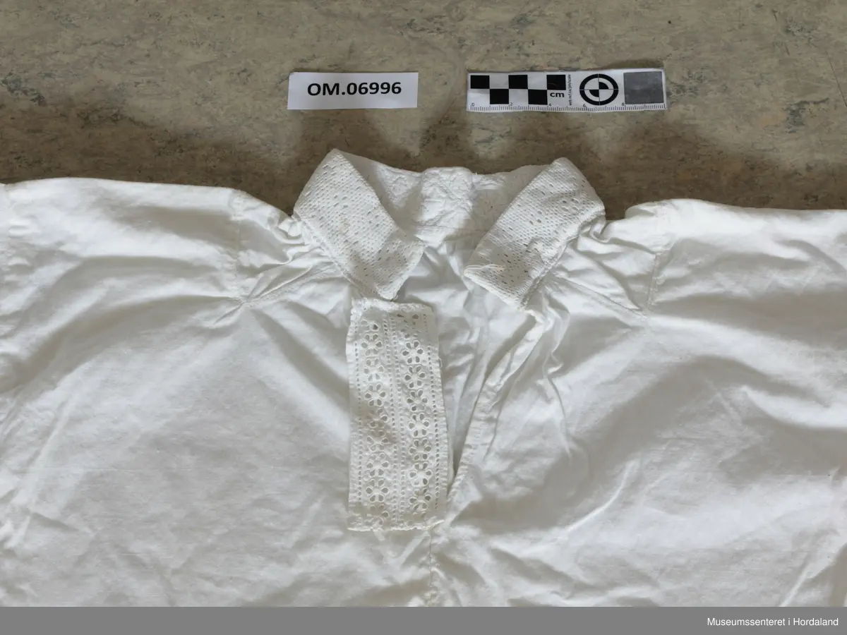 kvitsaum i halslinning, blondekant i bringa.