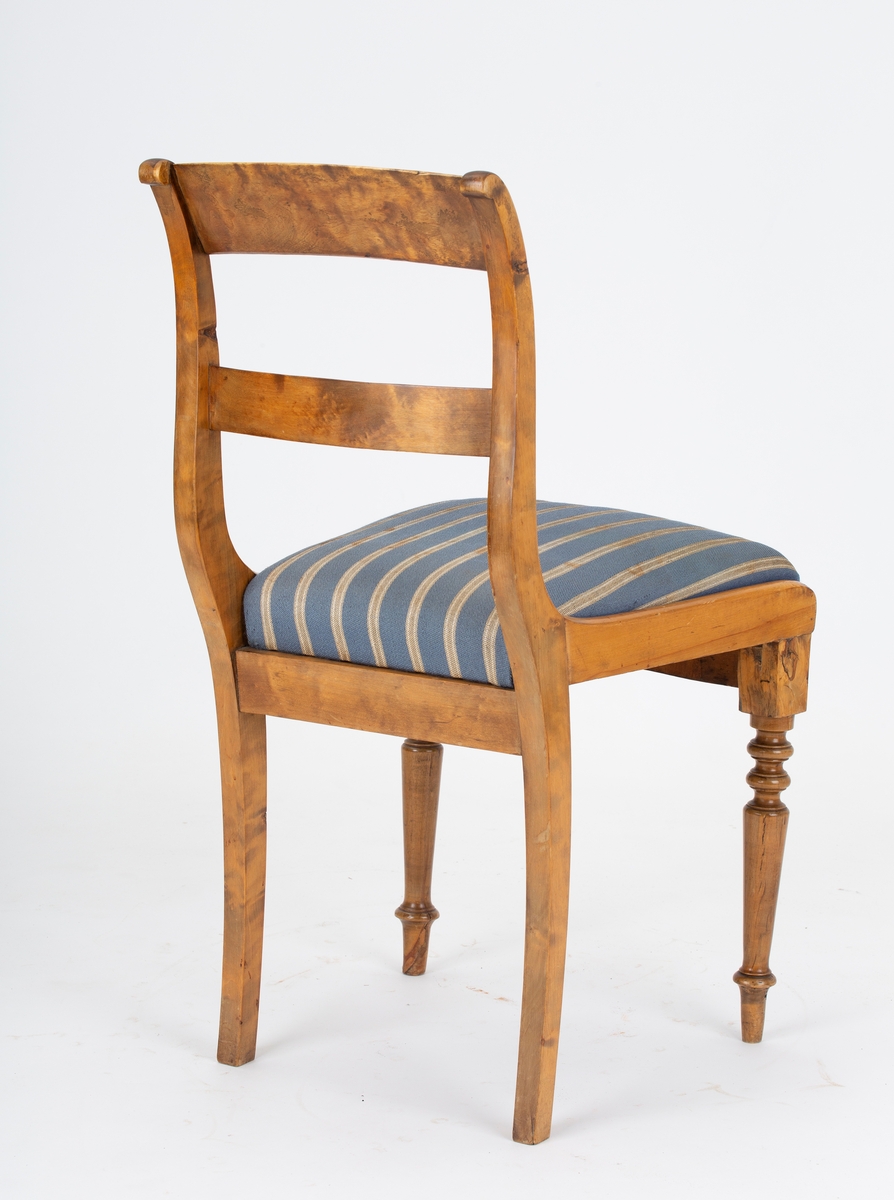 Stol, Biedermeier. Stoppet løst sete, gråblått ullstoff med grå og hvite smale striper. Dreide forben. Svai i rygg og bakben. 2 ryggspiler.
Kaffeflekker på stoltrekkene
