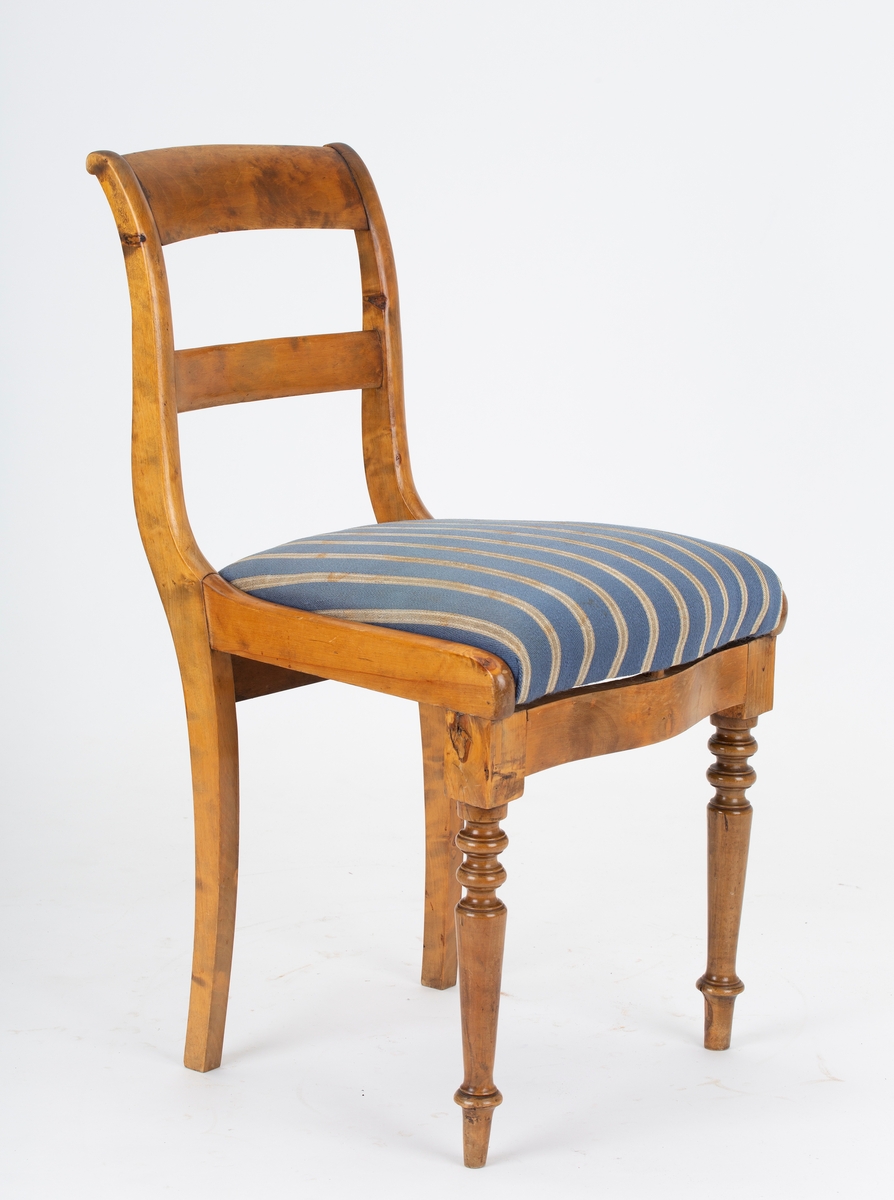 Stol, Biedermeier. Stoppet løst sete, gråblått ullstoff med grå og hvite smale striper. Dreide forben. Svai i rygg og bakben. 2 ryggspiler.
Kaffeflekker på stoltrekkene
