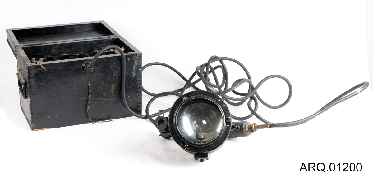 Signallampe/morselampe med batteri. Begge i svart farge. Batteriet ligger oppe i en trekasse som også er malt svart. Det hører også med en løs knott, som antagelig har falt av batteriet.
Det er en lampe av type Aldis Lantern produsert i Canada. Ved trykk på håndtaket bever speilet inne i lampen seg, med strøm og lys i lyspæren kan man da sende "SOS" ved nødsituasjoner. Lampen har et sikte på toppen.
Selve batteriet er tungt og består av 6 elementer satt sammen med ulike koblinger.
