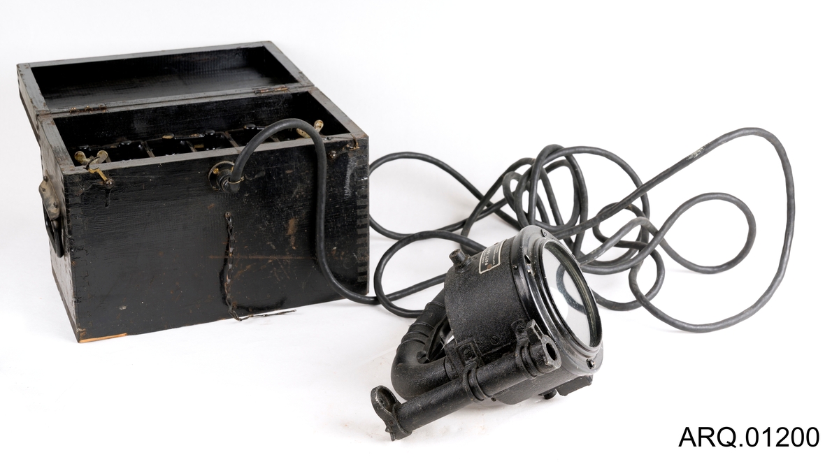 Signallampe/morselampe med batteri. Begge i svart farge. Batteriet ligger oppe i en trekasse som også er malt svart. Det hører også med en løs knott, som antagelig har falt av batteriet.
Det er en lampe av type Aldis Lantern produsert i Canada. Ved trykk på håndtaket bever speilet inne i lampen seg, med strøm og lys i lyspæren kan man da sende "SOS" ved nødsituasjoner. Lampen har et sikte på toppen.
Selve batteriet er tungt og består av 6 elementer satt sammen med ulike koblinger.
