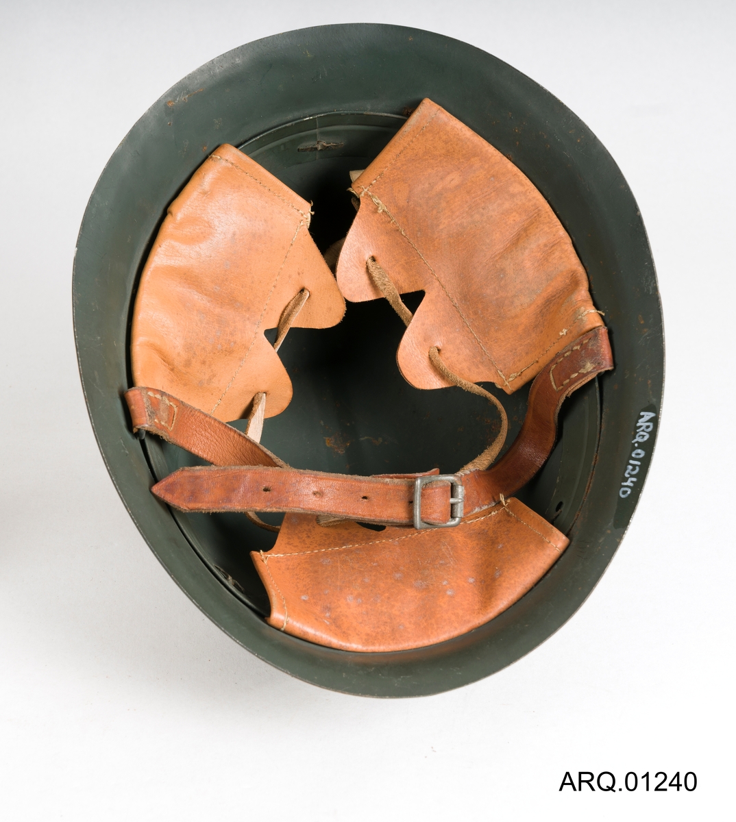 En Olivengrønn stålhjelm med skinninnlegg, festestropp i skinn med metallspenne og en stål-brem på innsiden av hjelmen.