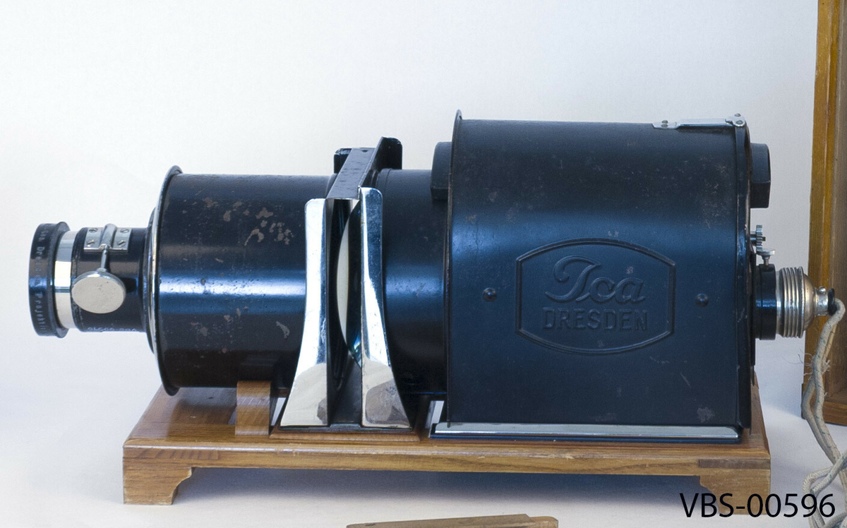 Lysbildefremviser apparat med 80 mm objektiv, 3 treskinne for bilder og trekasse. 
Gjenstanden er montert på en lakkert eikeplattform, med små ben og bue for å støtte sylinderen med de indre forstørrelseslinsene. Fast montert ujordet strømkabel og intakt indre lyspære.  Manuell framføring av lysbilder ved hjelp av treskinne beregnet for 35 mm lysbilder i ramme.