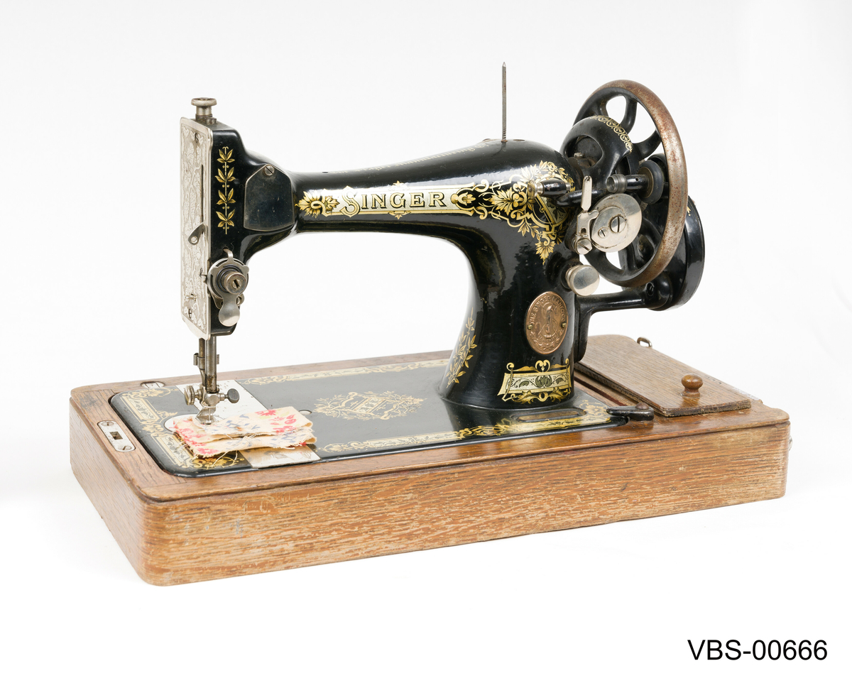 Maskinen har gullfarget mønster og skrift.
SINGER merkevare og påskriften "The Singer Manufackting company" pryder frontsiden med gullfarger motiver.