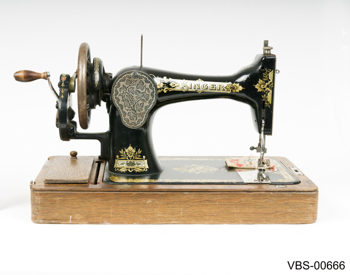 Maskinen har gullfarget mønster og skrift.
SINGER merkevare og påskriften "The Singer Manufackting company" pryder frontsiden med gullfarger motiver.
