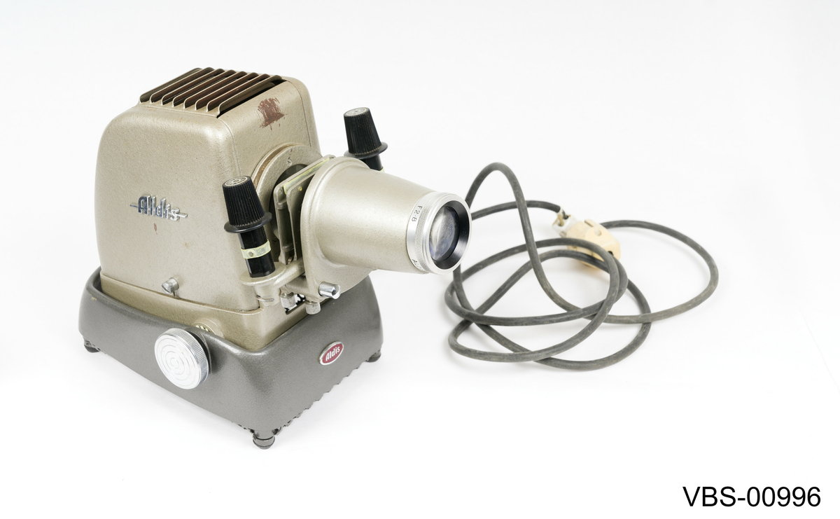 Fremviser Aldis, modell Star 300, i metall lakkert med sølvgrå farge. Objektiv med 10 cm linse og F 2.8.
Koffert i bronsefarge kartong (tekstil tekstur) med beige og hvitt stripete papirtrekk på innsiden. Håndtak i svart bakelitt og beslag i sølvfarget metall. Den har en liten intern papp skuff med trykklås som inneholder instruksjonspapirene av fremviser.