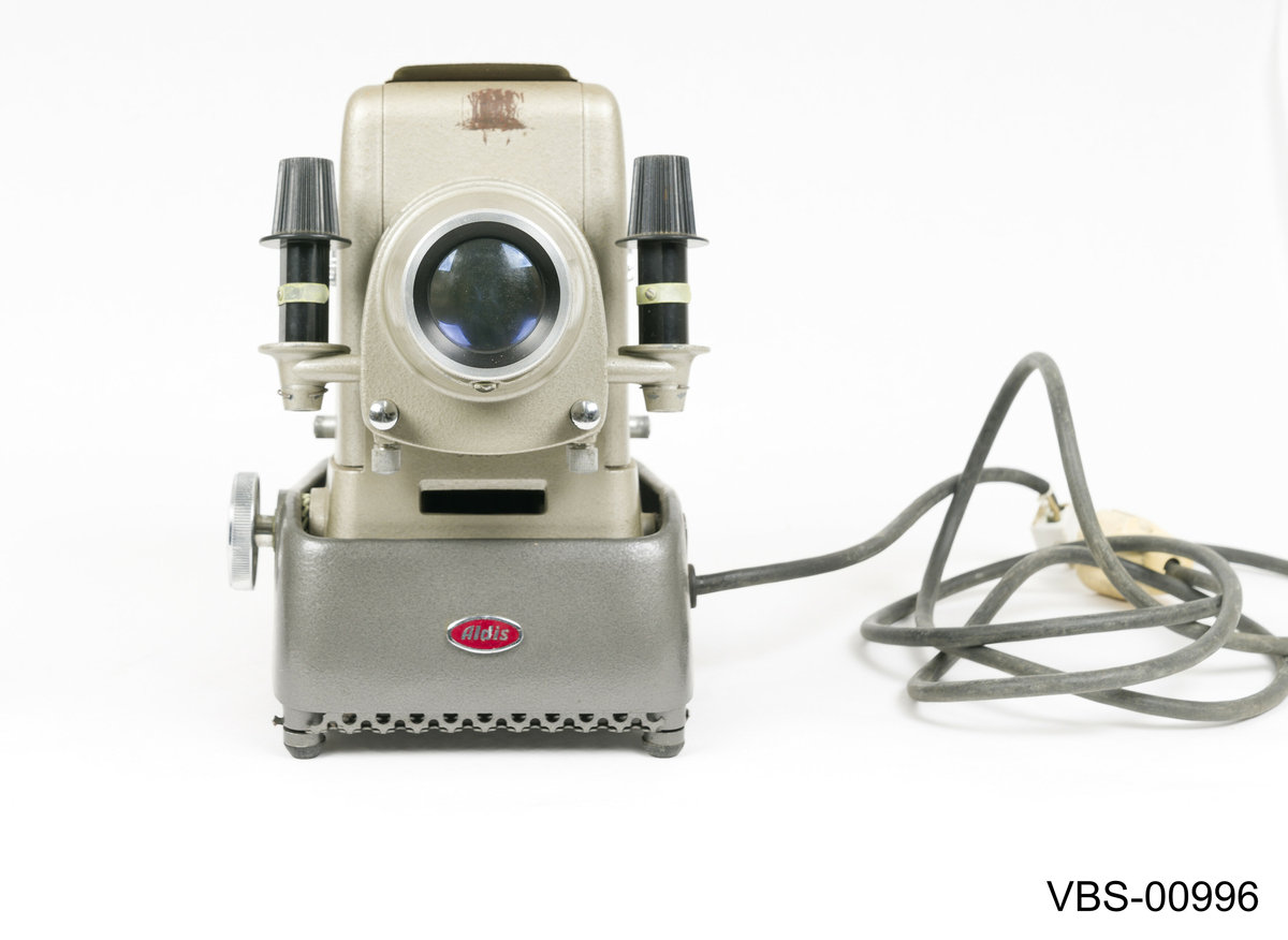 Fremviser Aldis, modell Star 300, i metall lakkert med sølvgrå farge. Objektiv med 10 cm linse og F 2.8.
Koffert i bronsefarge kartong (tekstil tekstur) med beige og hvitt stripete papirtrekk på innsiden. Håndtak i svart bakelitt og beslag i sølvfarget metall. Den har en liten intern papp skuff med trykklås som inneholder instruksjonspapirene av fremviser.