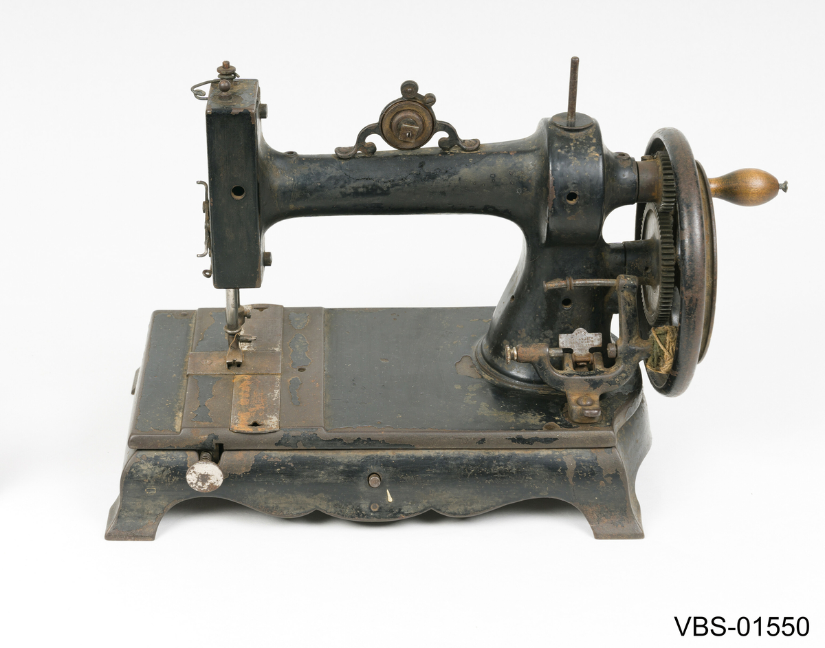 Symaskin med sveiv i svart jern. Den er festet med to hensgler på en solid sokkel av 6 cm i støpejern.   
Muligens produsert av GROVEN & BAKER (Boston, USA), produsenter siden 1851.