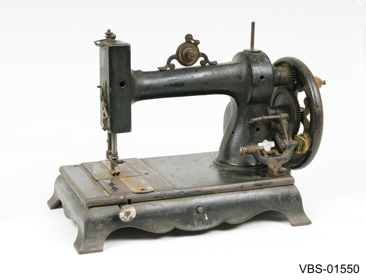 Symaskin med sveiv i svart jern. Den er festet med to hensgler på en solid sokkel av 6 cm i støpejern.   
Muligens produsert av GROVEN & BAKER (Boston, USA), produsenter siden 1851.