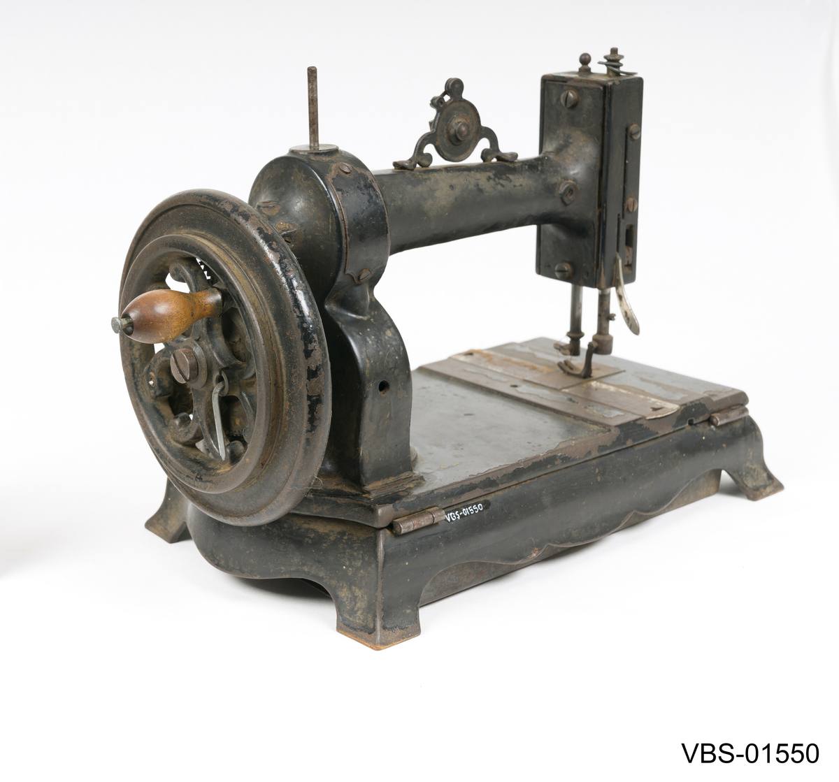 Symaskin med sveiv i svart jern. Den er festet med to hensgler på en solid sokkel av 6 cm i støpejern.   
Muligens produsert av GROVEN & BAKER (Boston, USA), produsenter siden 1851.