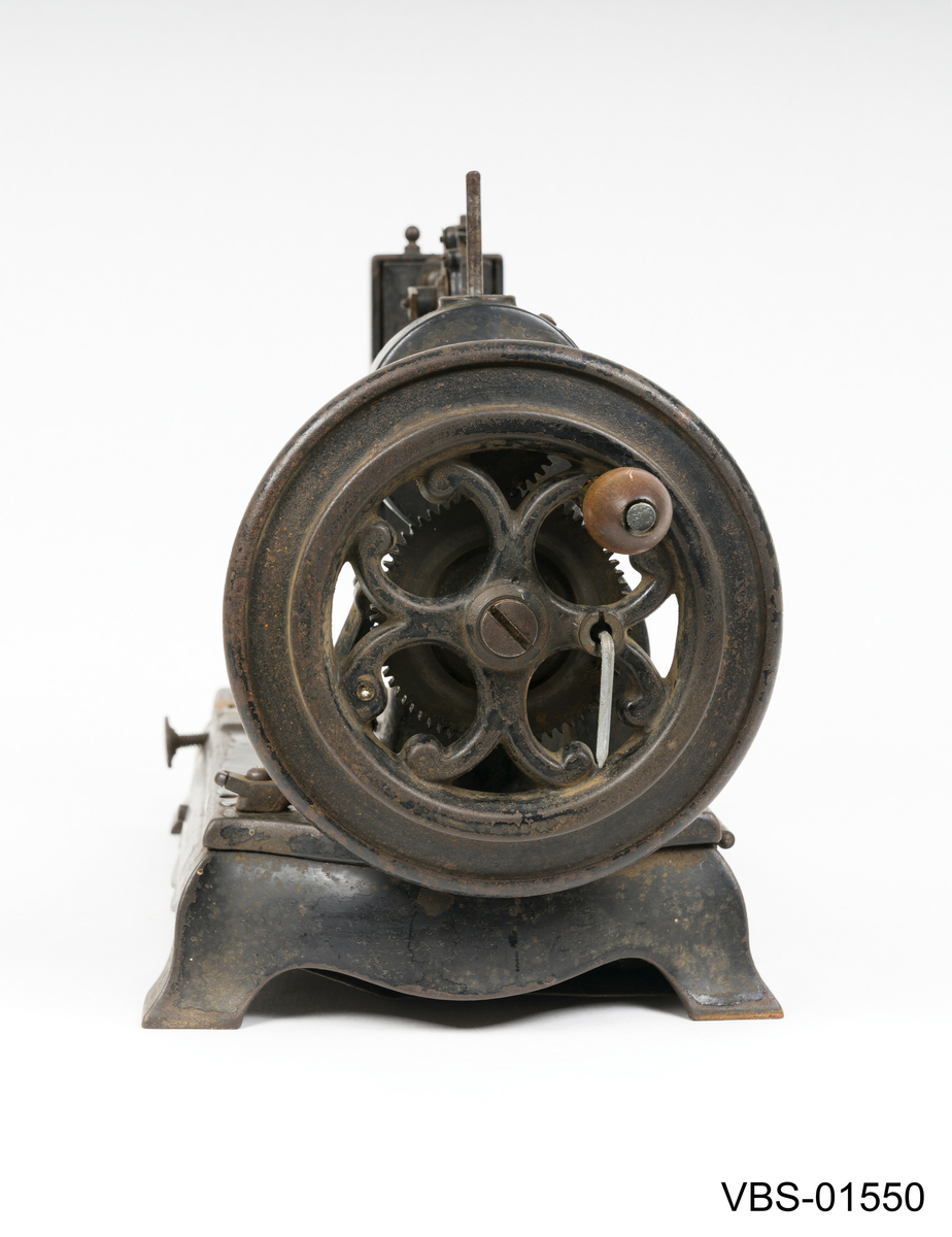 Symaskin med sveiv i svart jern. Den er festet med to hensgler på en solid sokkel av 6 cm i støpejern.   
Muligens produsert av GROVEN & BAKER (Boston, USA), produsenter siden 1851.