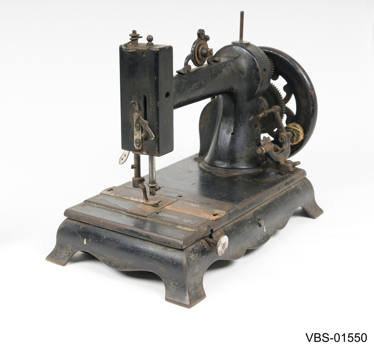 Symaskin med sveiv i svart jern. Den er festet med to hensgler på en solid sokkel av 6 cm i støpejern.   
Muligens produsert av GROVEN & BAKER (Boston, USA), produsenter siden 1851.