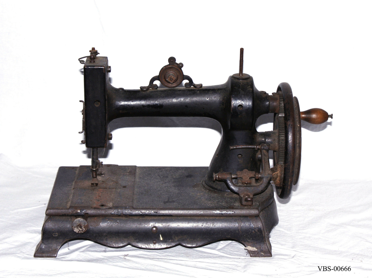 Symaskin med sveiv i svart jern. Den er festet med to hensgler på en solid sokkel av 6 cm i støpejern.   
Muligens produsert av GROVEN & BAKER (Boston, USA), produsenter siden 1851.