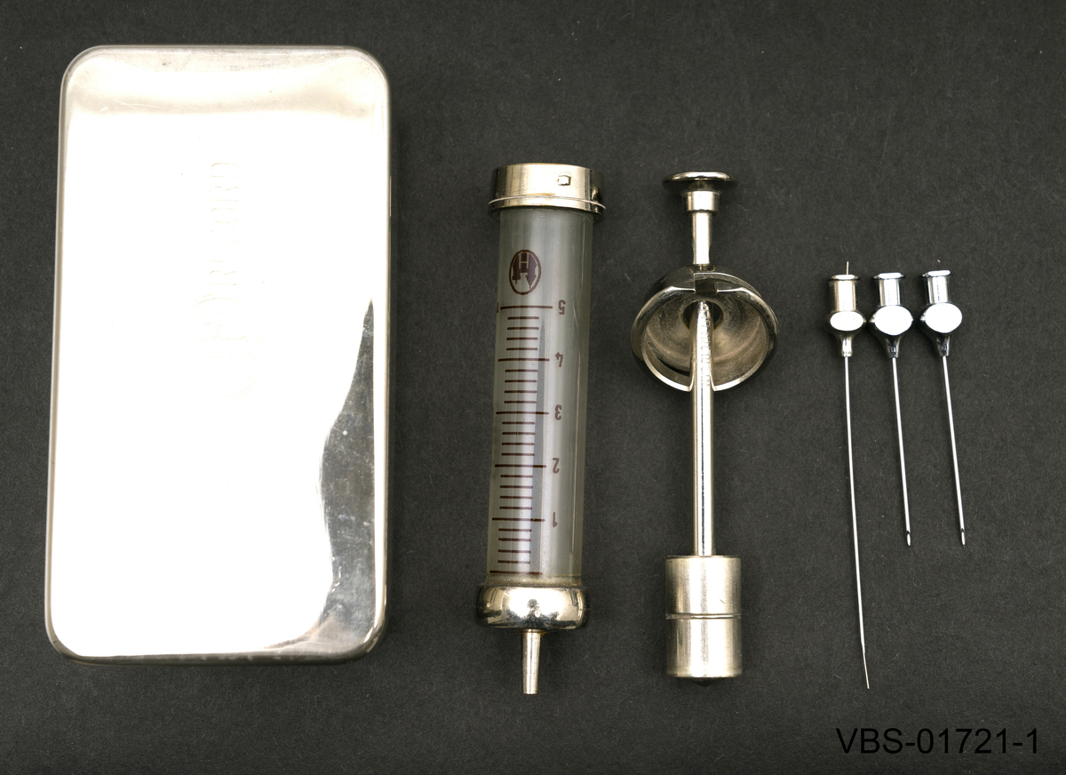 5ml sprøyte med beholder som ligger demontert i to deler, sammen med 3 sprøytespisser (nr. 12) og en stålsonde for å rengjøre nålen på innsiden.
Beholderen er en metallboks/etui i rusfritt stål med et stempel på lokket.