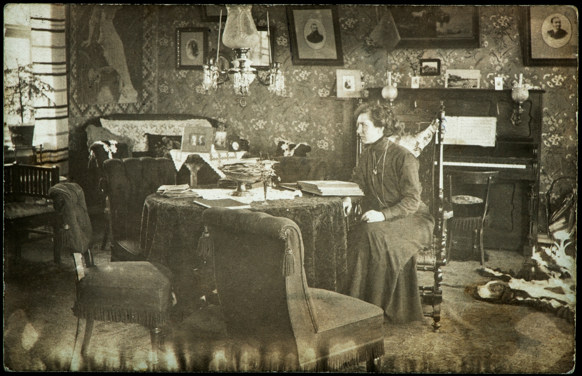 Interiør stue, fotograf Ragnhilda Eriksen ved et bord i sin egen stue.