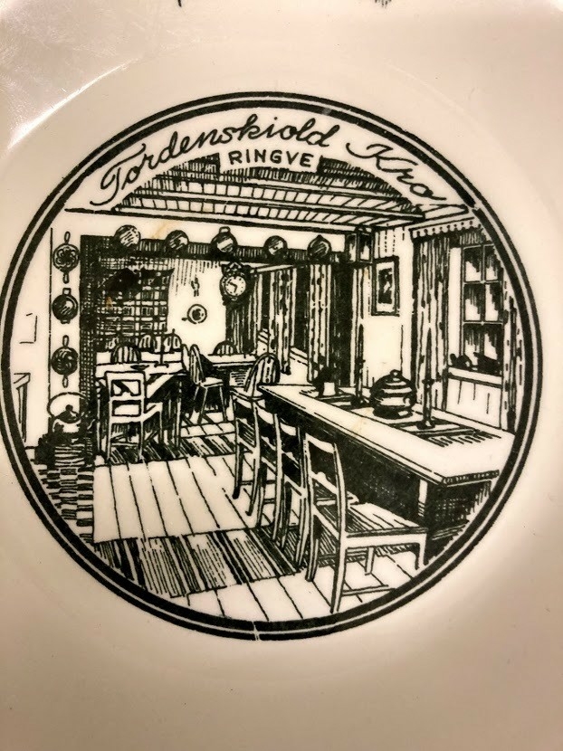 Avlang skål med håndtak, hull til oppheng. Ment for å henge på vegg. Dekorert på håndtak med helfigur av Tordenskiold. I skålens bunn dekorert med bilde av interiøret i "Tordnskiold-kro",