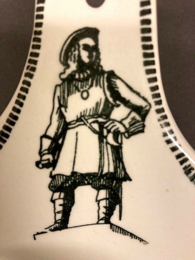 Avlang skål med håndtak, hull til oppheng. Ment for å henge på vegg. Dekorert på håndtak med helfigur av Tordenskiold. I skålens bunn dekorert med bilde av interiøret i "Tordnskiold-kro",