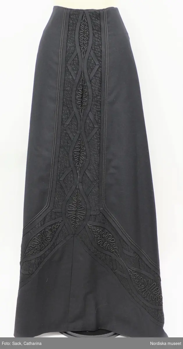 Ordered by Alice Bexelius née Eales (1865–1952), a merchant’s wife. Delivered ca. 1902–1910. Black two-piece wool dress in the fashionable S-shaped silhouette. High-necked, corseted bodice and floor-length skirt with train. Discreet, decorative soutache ribbon decorations and contrasting areas of crêpe de chine and transparent chiffon.