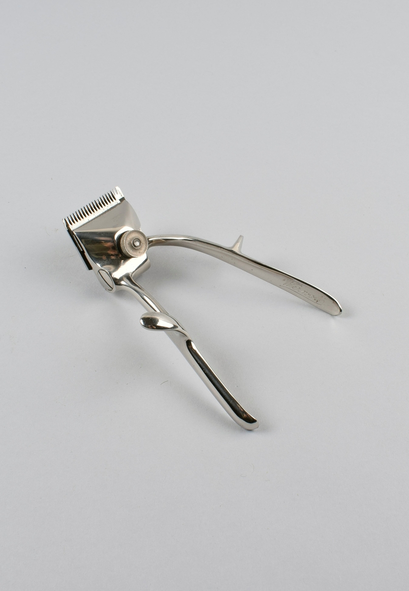 Manuell hårklipper med to skaft med fingerstøtte. Det ene skaftet beveges sideveis for å oppnå klippefunksjon på klippehodet. Ligger i originaleske med tilhørende deksel i metall.
