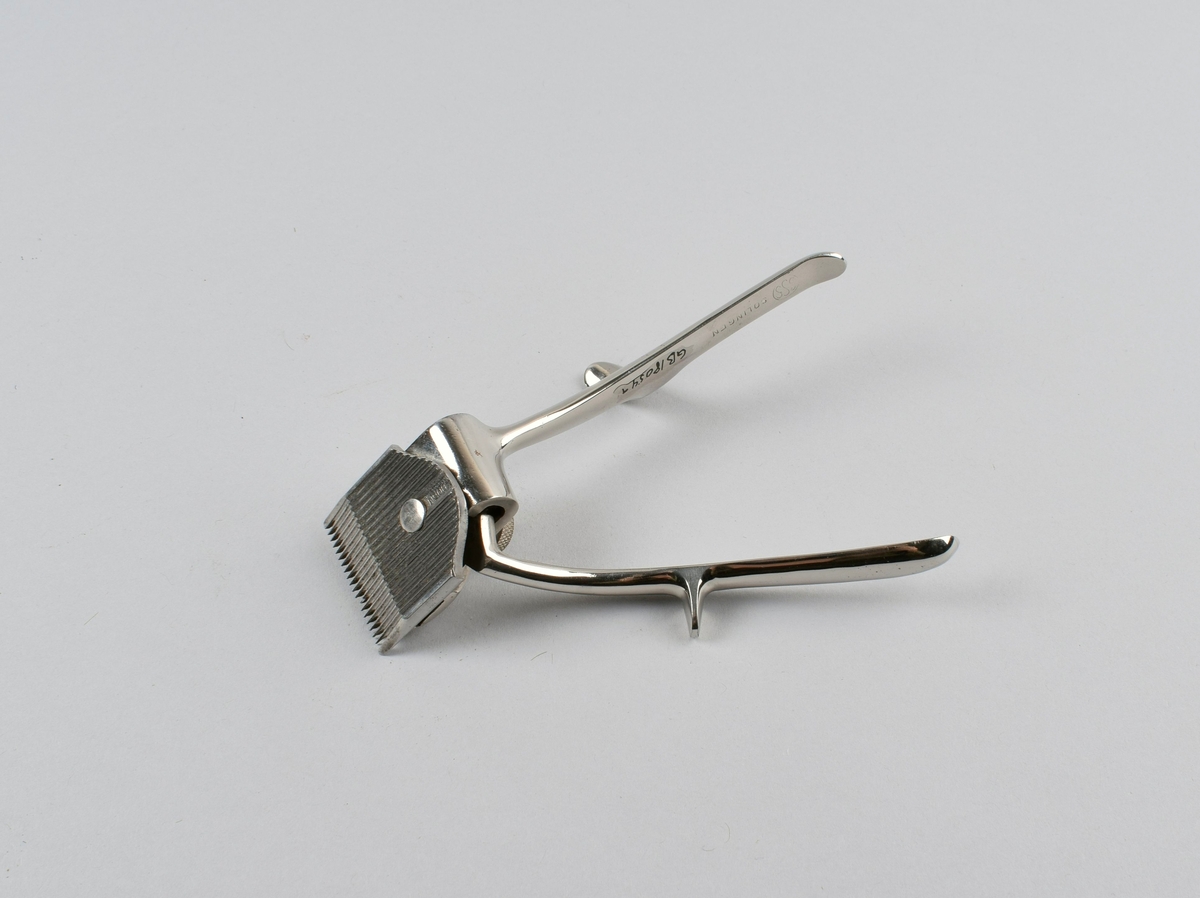 Manuell hårklipper med to skaft med fingerstøtte. Det ene skaftet beveges sideveis for å oppnå klippefunksjon på klippehodet. Ligger i originaleske med tilhørende deksel i metall.
