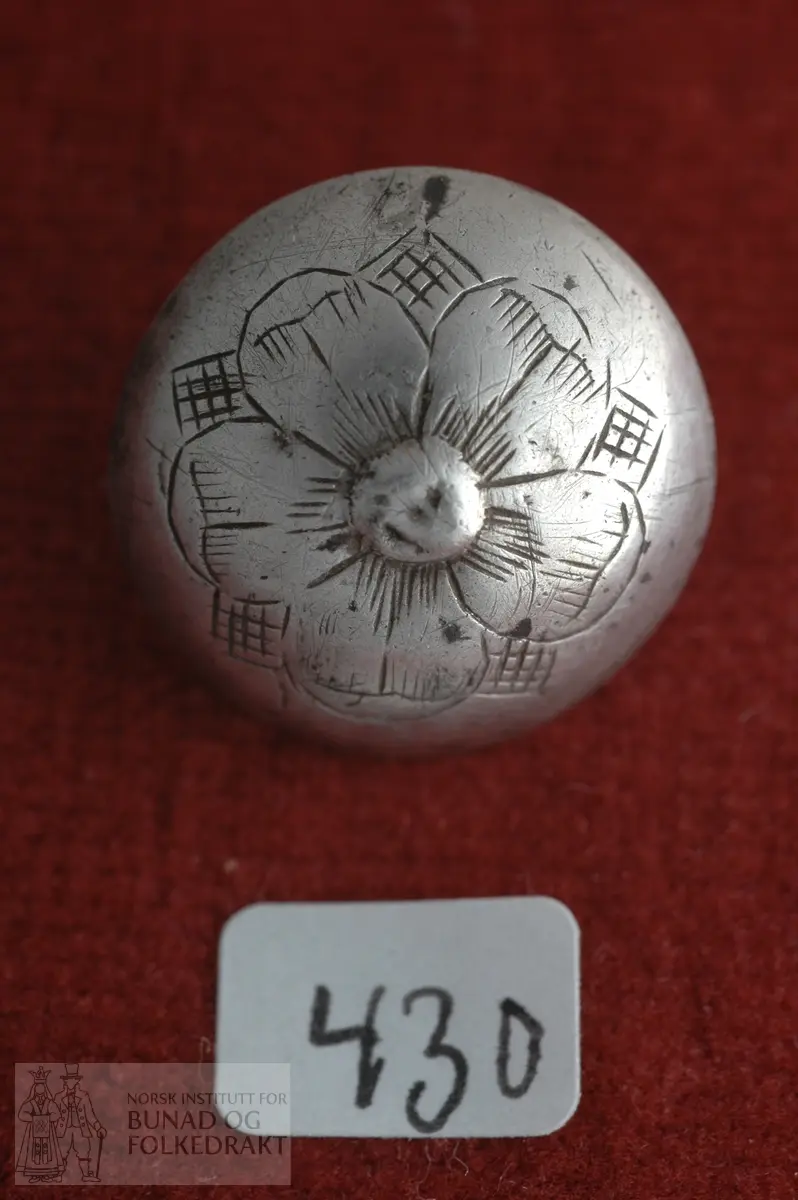 Kuven sølvknapp med gravert mønster. Plate og pålodda hempe på baksida. Merka S M  Diameter:  2 cm.