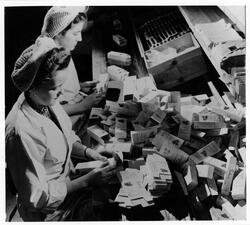 Två kvinnor viker kartonger på Suchards Chokladfabrik.