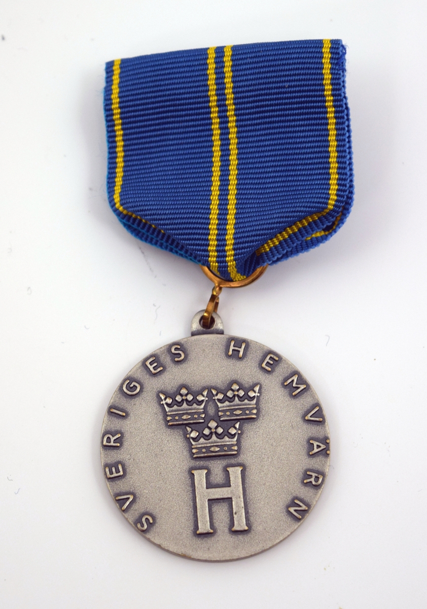 Hemvärnets förtjänstmedalj i silver. Rund medalj i silver men sidenripsband, blått med fyra gula streck. Ena sidan med hemvärnets emblem i form av bokstaven "H" med tre kronor över samt texten: "Sveriges hemvärn". På andra sidan texten: "Västkustens Marinkommando, för förtjänster om hemvärnet" samt motiv av två sköldar, en med Göteborgs stadsvapen samt en med Bohusläns vapen.