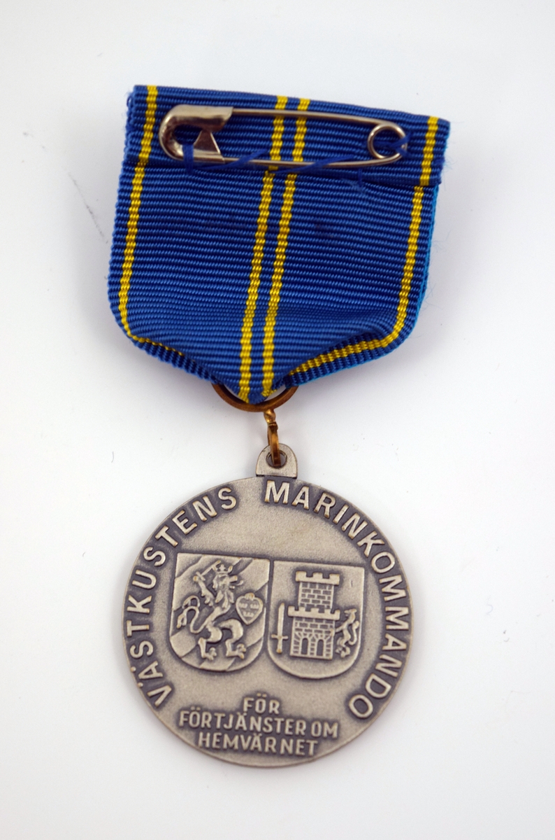 Hemvärnets förtjänstmedalj i silver. Rund medalj i silver men sidenripsband, blått med fyra gula streck. Ena sidan med hemvärnets emblem i form av bokstaven "H" med tre kronor över samt texten: "Sveriges hemvärn". På andra sidan texten: "Västkustens Marinkommando, för förtjänster om hemvärnet" samt motiv av två sköldar, en med Göteborgs stadsvapen samt en med Bohusläns vapen.