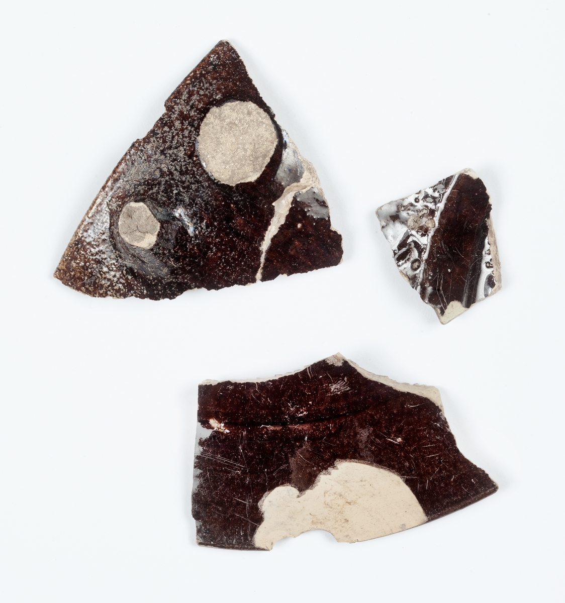 Delar av kärl. 10 stycken keramikfragment. Fyra brunglaserade bitar till mindre kärl, fem bitar grönglaserat lergods samt en vitglaserad bit med blå dekor.