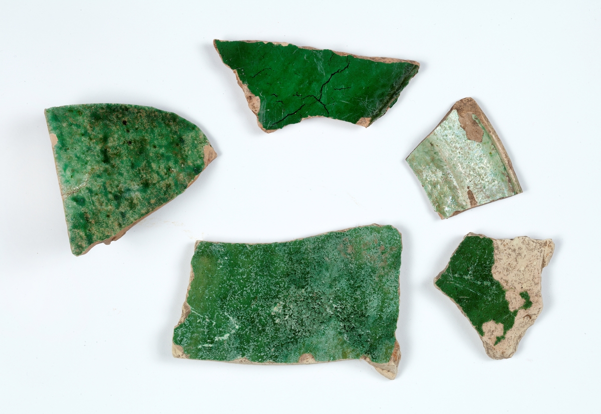 Delar av kärl. 10 stycken keramikfragment. Fyra brunglaserade bitar till mindre kärl, fem bitar grönglaserat lergods samt en vitglaserad bit med blå dekor.